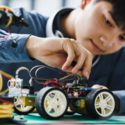 Asian teenager students doing robot arm and robotic cars homework project in house disassemble the circuit and coding. technology of robotics programing and STEM education concept.